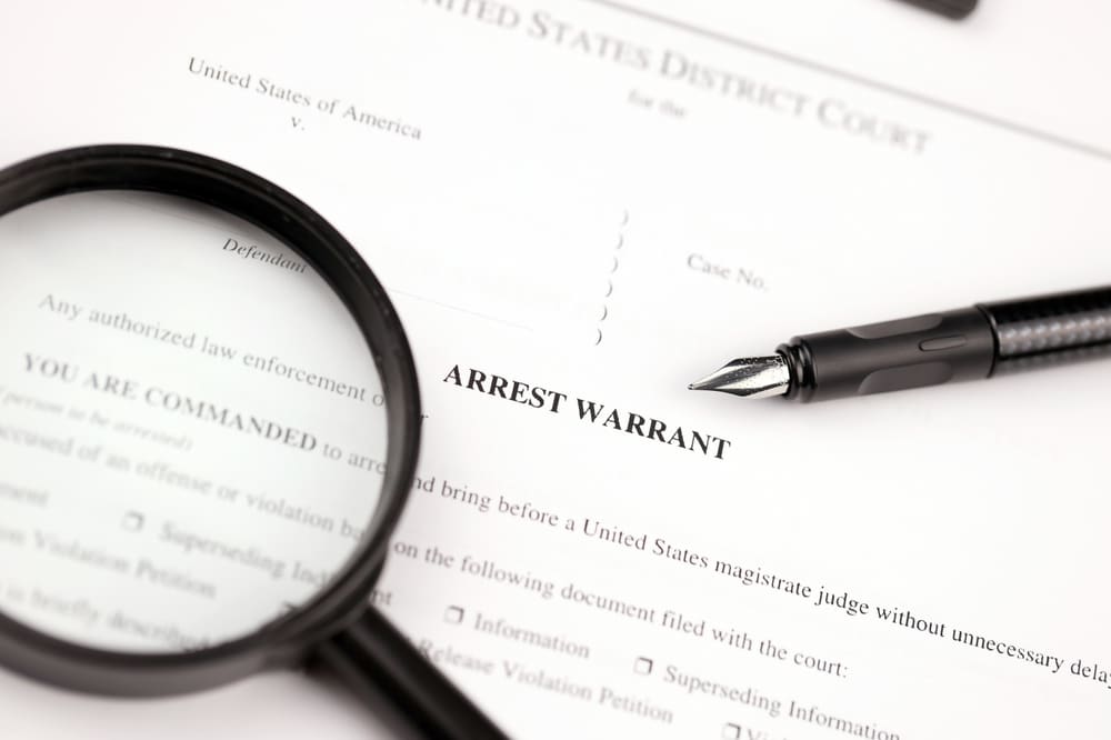 District Court Arrest Warrant court papers on A4 tablet lies on office table with pen and magnifying glass close up