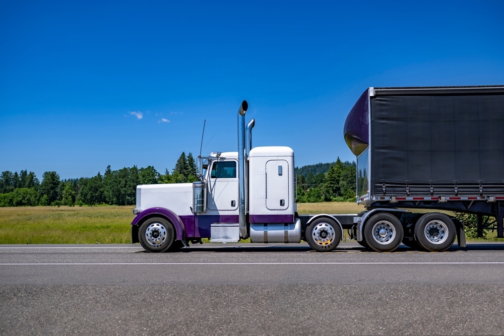 Industrial carrier white and purple classic big rig semi truck tractor with extended cab for truck driver rest transporting cargo in tented dry van black semi trailer running on the highway road