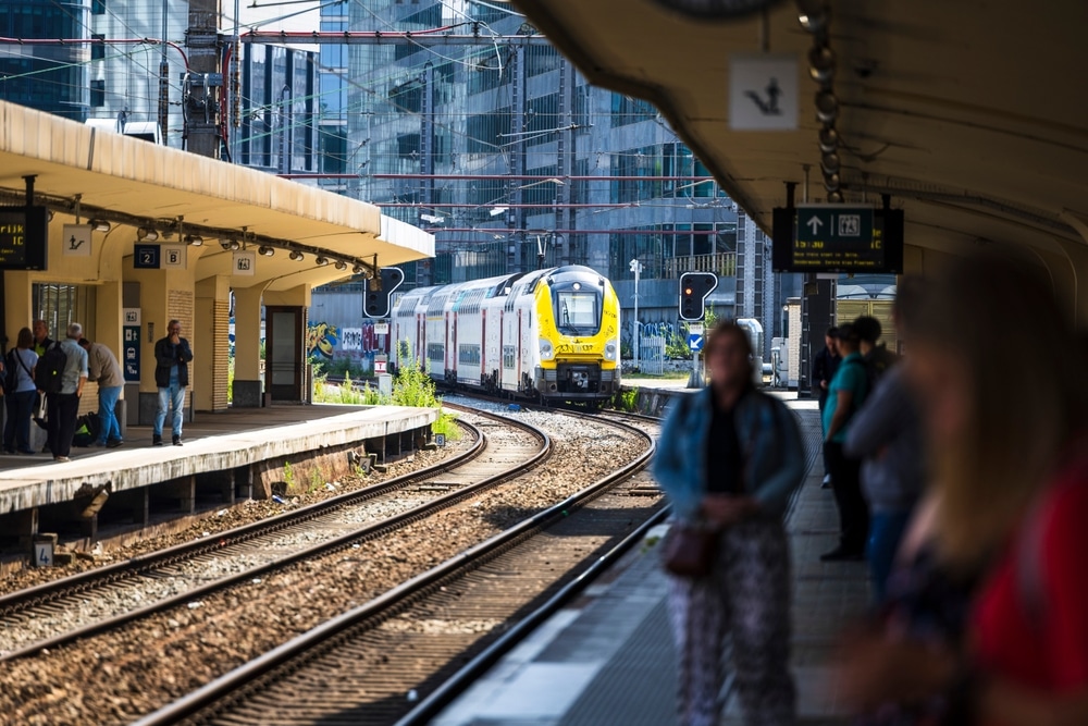 Brussels Belgium 2025-07-11
A Belgian NMBS SNCB yellow and grey train with graffiti arrives at a busy station platform.