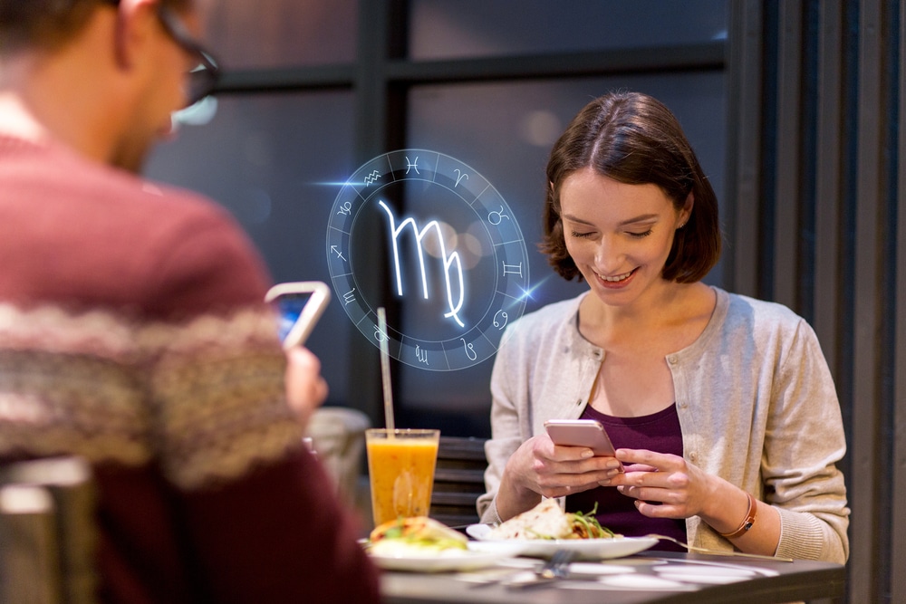 technology, astrology, horoscope and people concept - happy couple or friends with smartphones and scorpio zodiac sign having dinner at restaurant