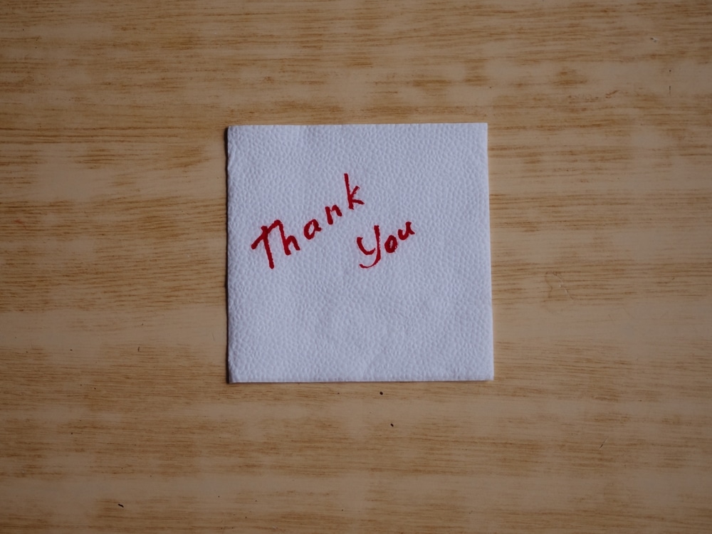 Horizontal close up of a handwritten "Thank You" on a paper napkin.