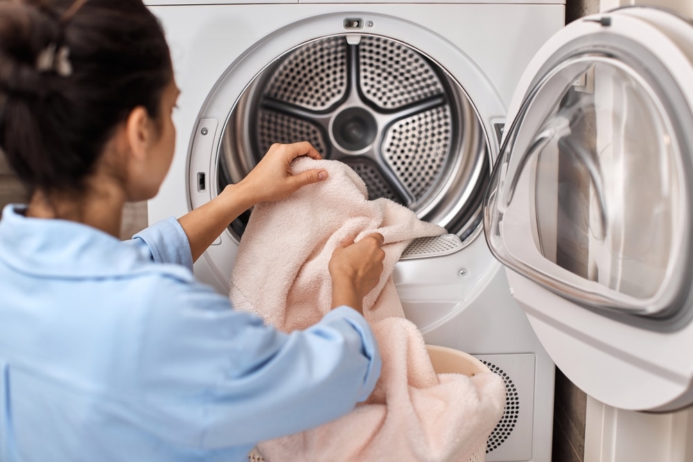 woman put pastel cotton towel in automatic washing machine with open door