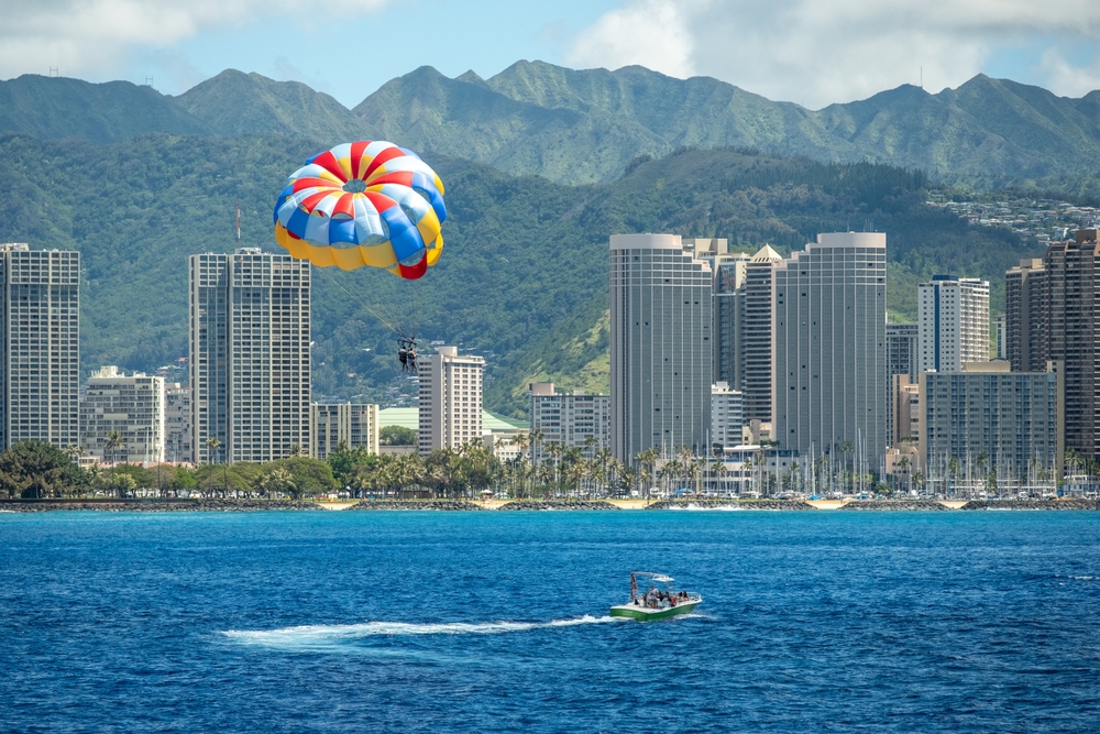 Parasail hovers over boat and buildings on the edge of Waikiki, captured March 15, 2019 in Honolulu, Hawaii, USA