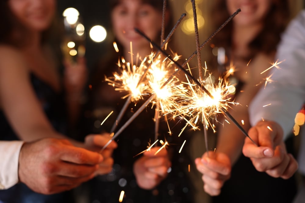 Friends celebrating New Year with sparklers and wine glasses indoors, closeup
