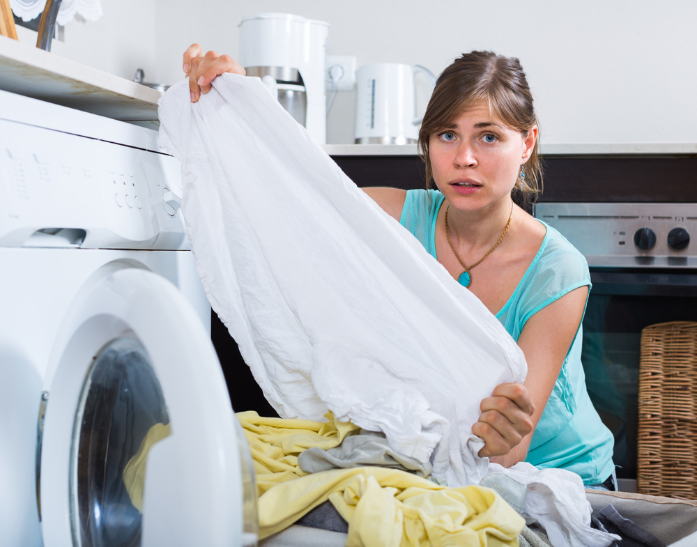 Upset maid looking at clothes with persistent stains after laundry at house