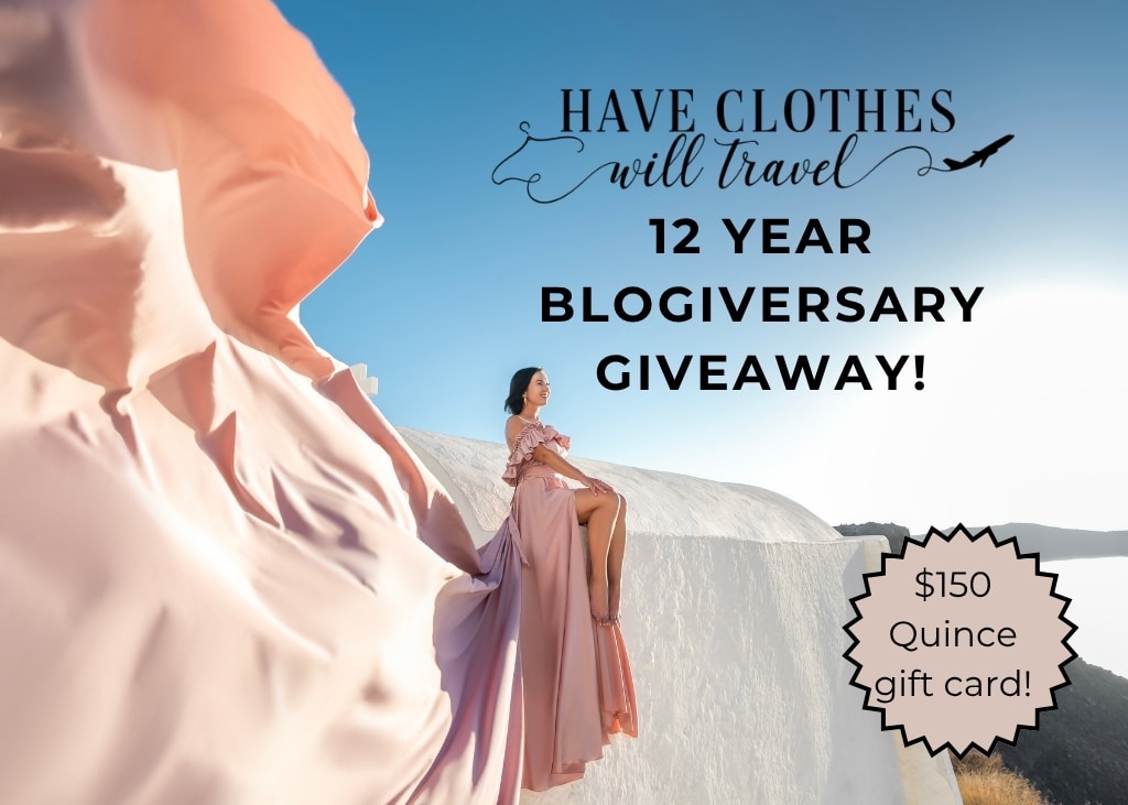 Lindsey Puls of Have Clothes, Will Travel sitting on a white ledge with a pink flying dress in Santorini Greece