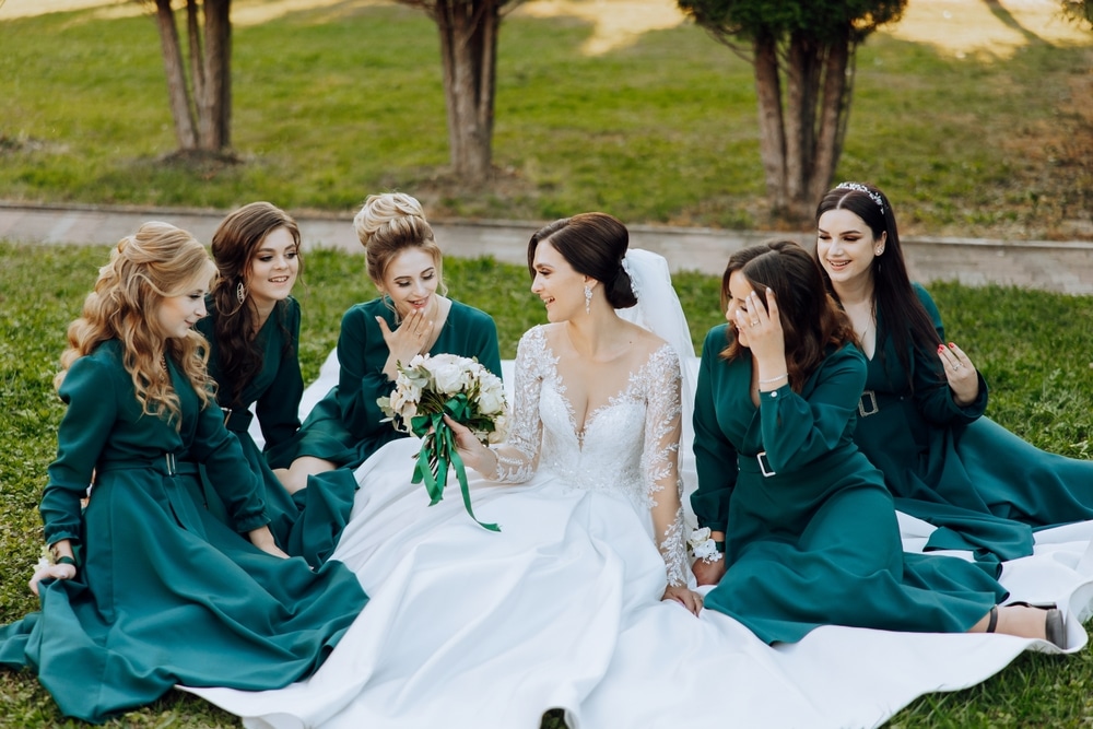 Wedding photography. A brunette bride in a wedding dress and her friends in emerald dresses pose with a bouquet in nature. Sunlight. Style. Autumn wedding. Friendship. A group of young girls.