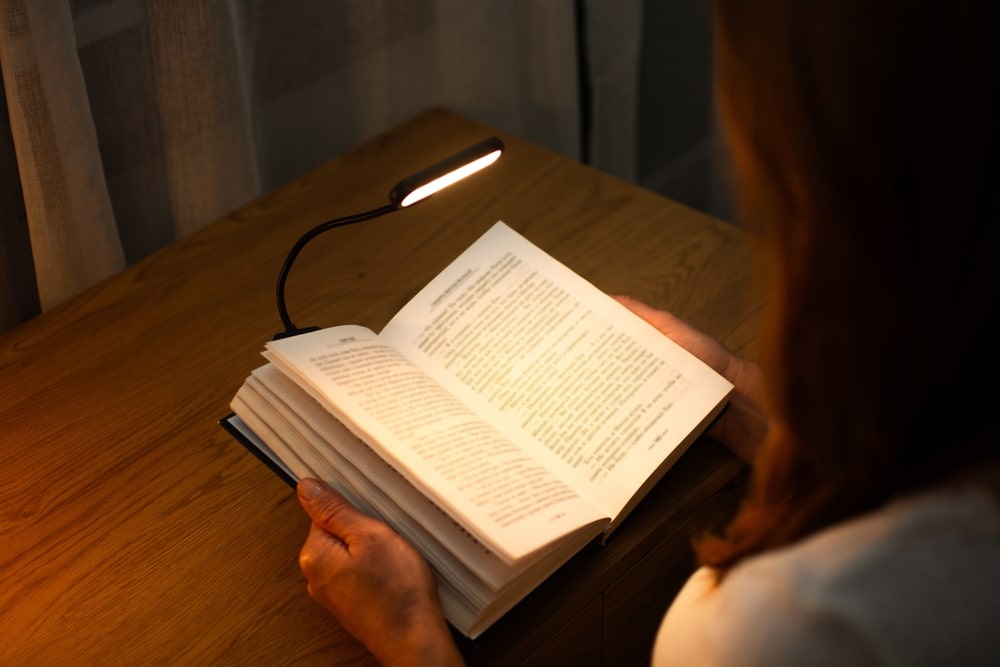 Reading a book at a wooden desk in the evening with the help of a convenient clip-on lamp. Eye protection in the dark and suitable warm light for health. High quality photo