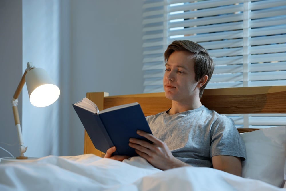 Man reading book before sleep with night lamp at home